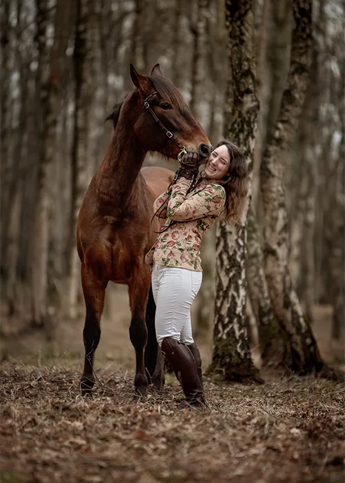 Junge Frau in Reitstiefeln schmiegt sich im Birkenwald bei Bremen Kopf an Kopf an ihr braunes Pferd — Fotoshooting mit Pferd in Bremen von Ines Arnshoff.