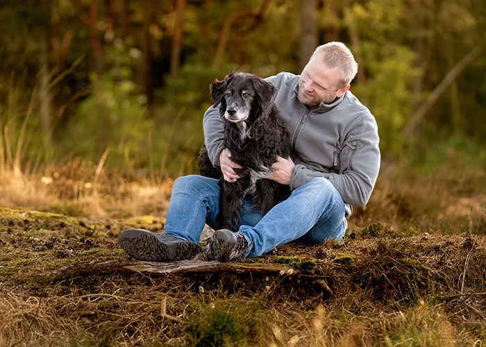 Mann sitzt im Tister Bauernmoor und hält seinen schwarzen Collie Seniorhund im Arm, Tierfotografie in Bremen von Ines Arnshoff.