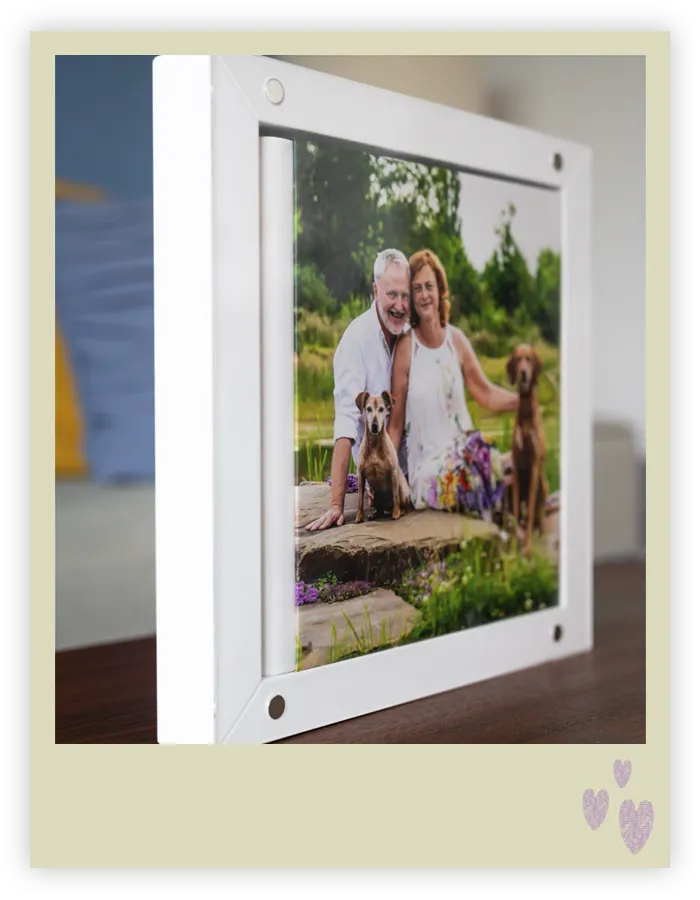 Gerahmter Print im weißen Acryl-Magnetrahmen zeigt ein Paar mit seinen zwei Hunden, aufgestellt auf einem Sideboard, Fotoprodukt von Hundefotografin Ines Arnshoff aus Bremen.