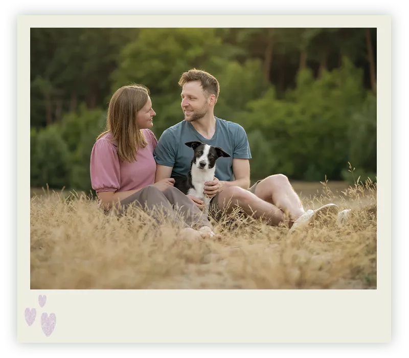 Junges Paar sitzt im sommerlichen Feld mit seinem schwarz-weißen Terrier-Mix, Hundefotografie in Bremen und Niedersachsen von Ines Arnshoff.