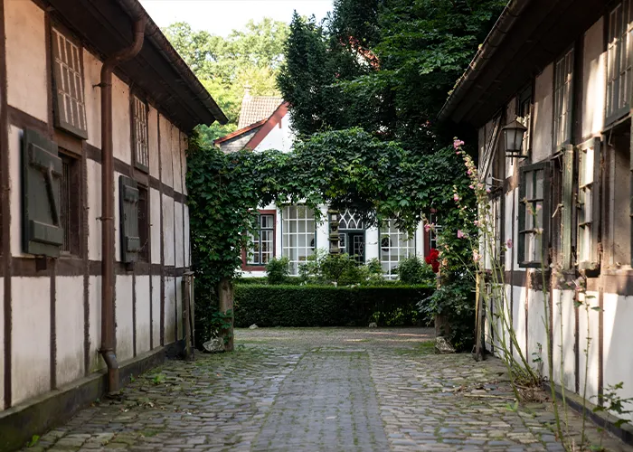 Stille Fachwerkgasse mit Kopfsteinpflaster und Stockrosen am Hubertus Reitverein in Bremen Oberneuland — eine unscheinbare Fotoshooting-Location, bevor hier ein besonderes Pferdefoto entsteht.