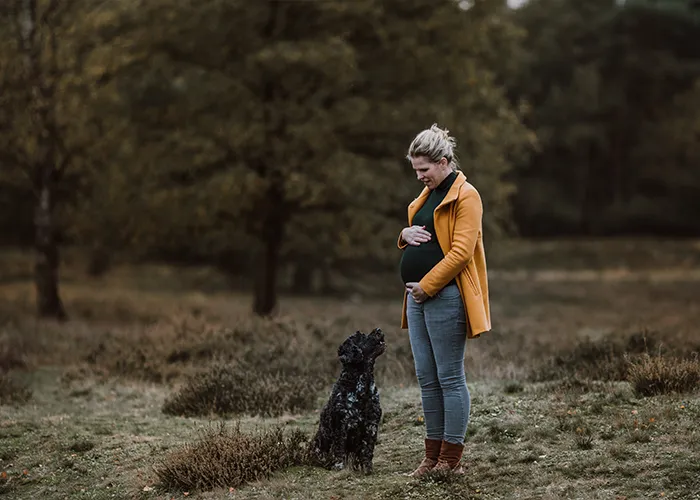 ochschwangere Ines Arnshoff steht in der Heide, ihre Hündin Winnie sitzt vor ihr und schaut zu ihr hoch.