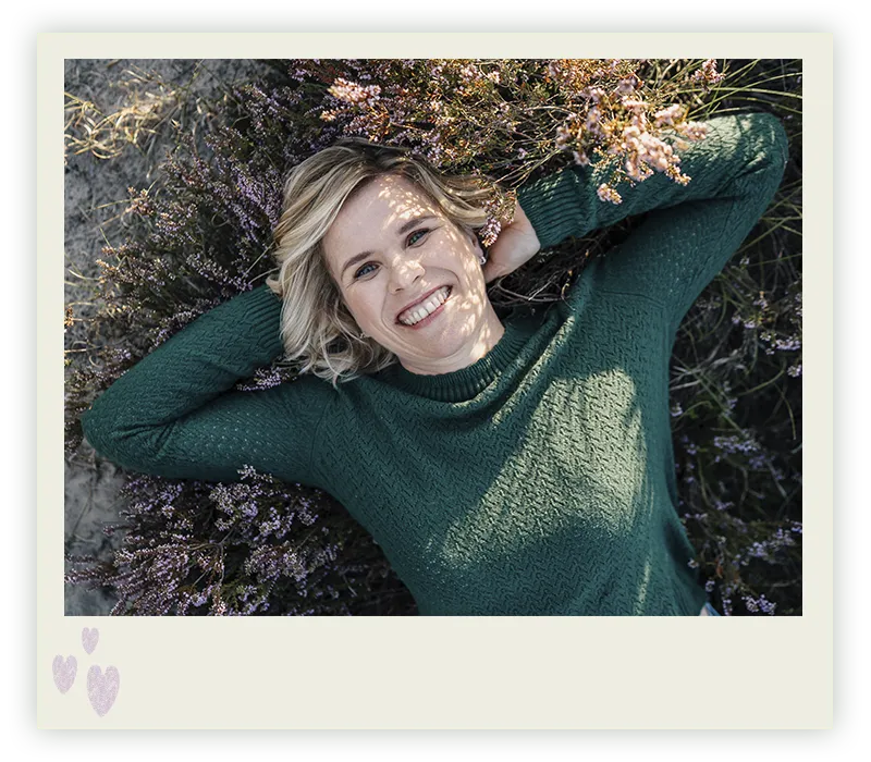 Ines Arnshoff liegt lachend im blühenden Heidekraut, die Arme hinter dem Kopf verschränkt in die Kamera nach oben blinkend